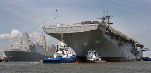 Tugboats guide the amphibious assault ship America (LHA 6) to her berthing place on Monday at Ingalls Shipbuilding. The Ingalls-built amphibious transport dock Arlington (LPD 24) can be seen in the background. УДК типа "Америка"